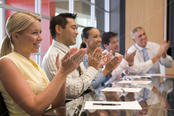 Five businesspeople at boardroom table applauding and smiling