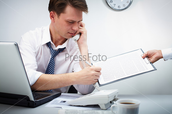 Portrait of confident businessman calling by phone while signing the contract held by his secretary