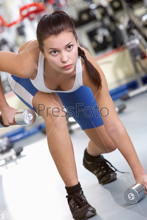 Photo of sporty brunette in sportswear taking barbells from the floor in gym