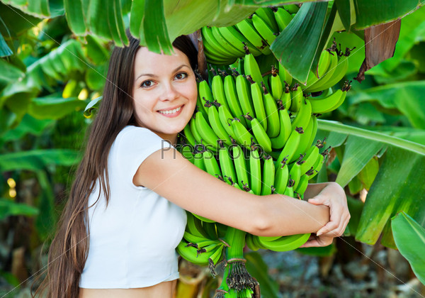 Улыбающаяся молодая женщина обнимает бананы, растущие на дереве