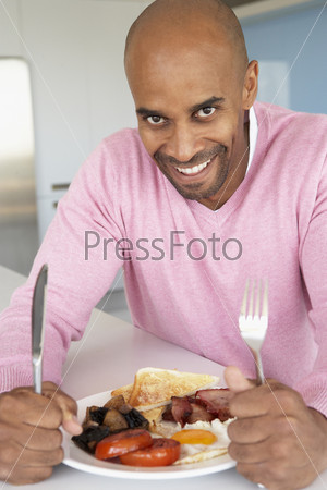 Темнокожий мужчина ест яичницу с беконом