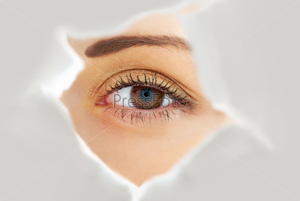 Image of human eye looking through hole in white paper sheet