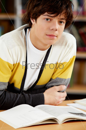 Portrait of clever student sitting in front of open book in college library