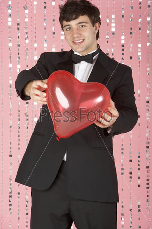 Молодой человек в смокинге держит в руках шарик в форме сердечка