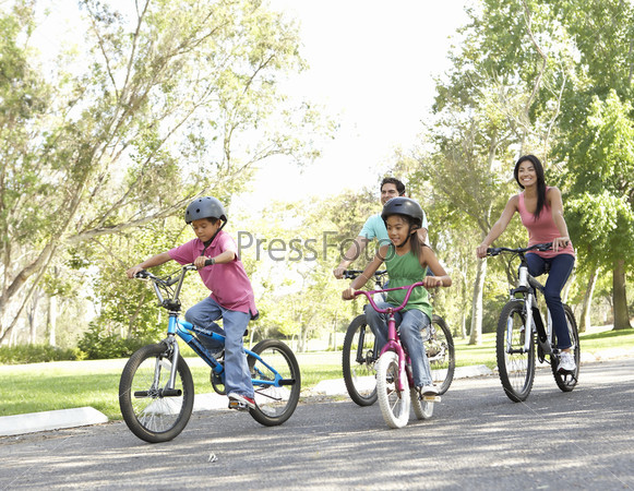 Мама, папа и дети катаются по парку на велосипедах