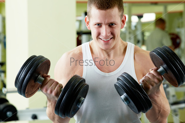 Portrait of sporty man with two dumbbells looking at camera