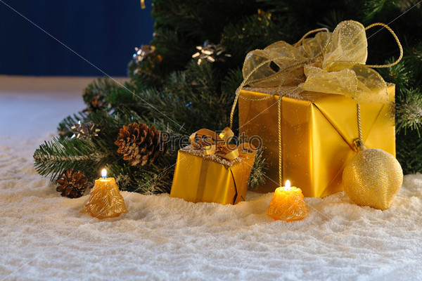 golden Christmas gift boxes with burn candles under decorated fir on snow