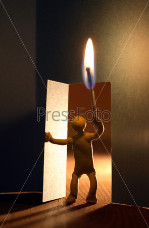 Yellow plasticine man with lighting match entering to dark room. Conceptual composition with open door made from paper, stock photo