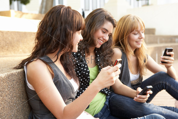 Девочки-подростки сидят на ступеньках с мобильными телефонами в руках