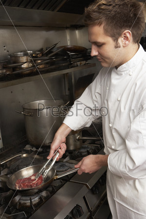 Male Chef Preparing Meal On Cooker In Restaurant Kitchen