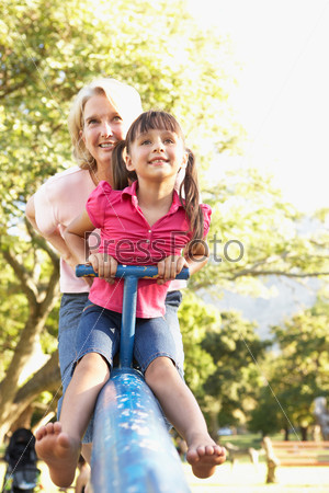 Grandmother And Granddaughter Riding On See Saw In Playground, stock photo