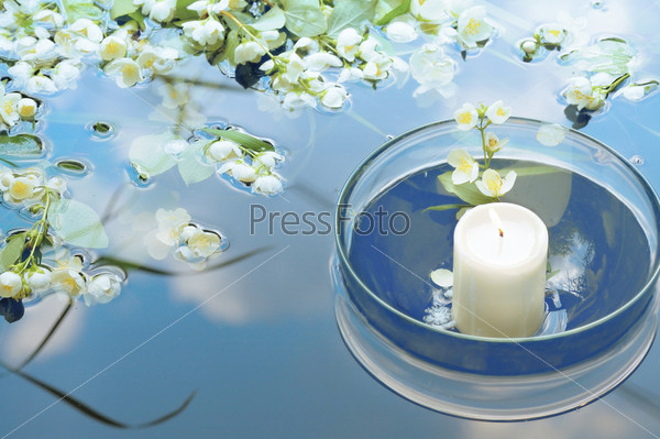 white candle in glass floating in water with jasmin reflecting sky