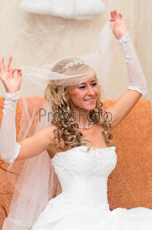 Portrait of a young beautiful bride with blonde curly hair in a white low-necked dress with a veil