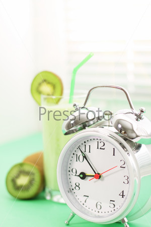 Kiwi juice in a glass and alarm clock on a light background