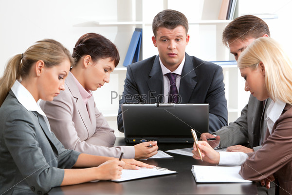 Photo of business group sitting at workplace and working with papers
