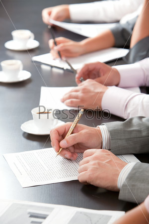 Close-up of line of hands with pens over papers on the table