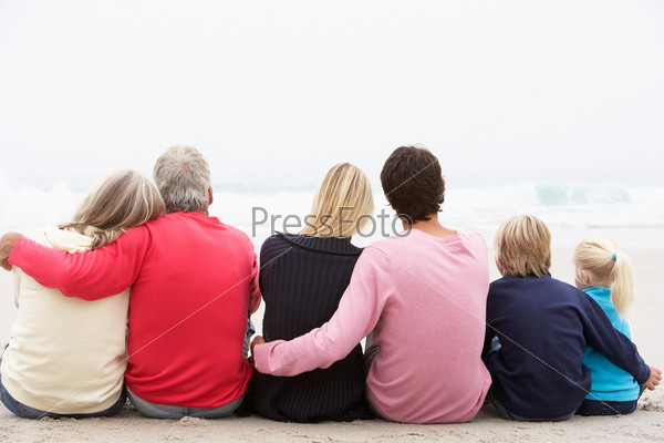 Back View Of Three Generation Family Sitting On Winter Beach Together