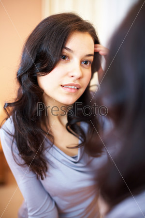 Portrait of pretty brunette looking in mirror while touching her face