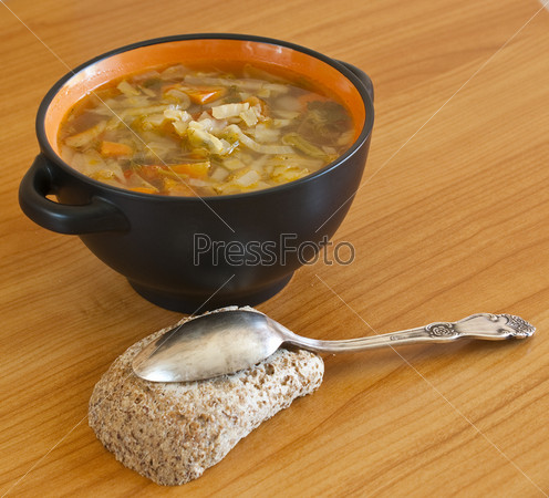 a bowl of vegetable soup with a silver-spoon and a piece of bread on the table