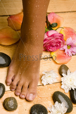 bronzed wet foot on board floor with stones, flowers, rose and rose-petals