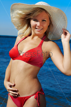 beautiful slvonic blonde girl posing in red bikini and summer hat, sea on background