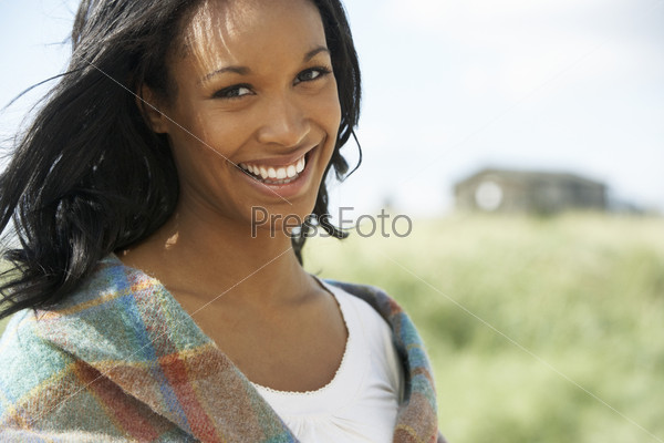Улыбающаяся молодая женщина на пляже, закутанная в шаль