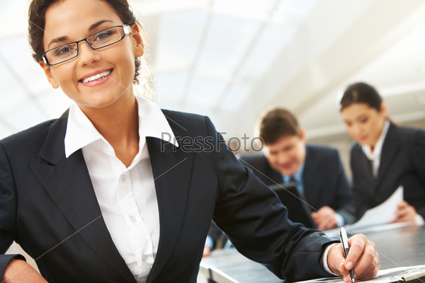 Portrait of happy leader with busy companions working with papers at background