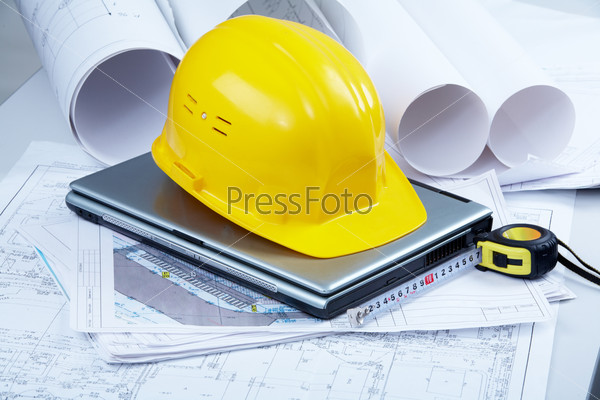 Image of helmet, blueprints, laptop and mechanical tools at workplace