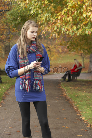 Задумчивая девушка с мобильным телефоном в осеннем парке