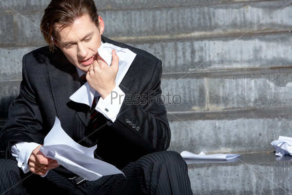 Расстроенный бизнесмен изучает документы, сидя на лестнице