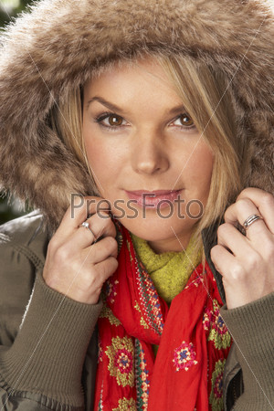 Fashionable Woman Wearing Parka Coat And Scarf In Studio In Front Of Christmas Tree