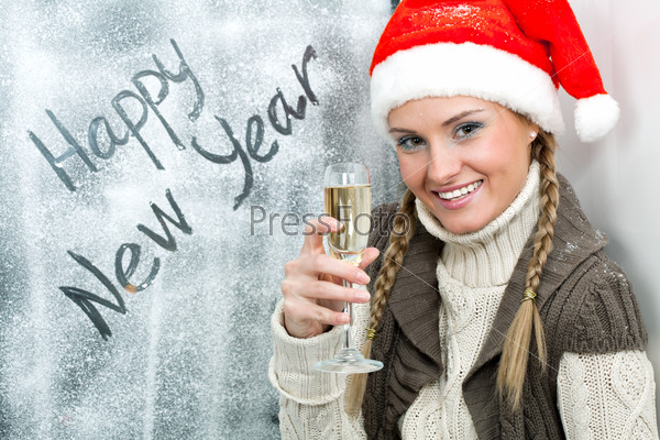 Happy female in Santa cap with flute of champagne looking at camera