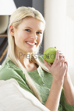 Женщина отдыхает на диване с яблоком в руке