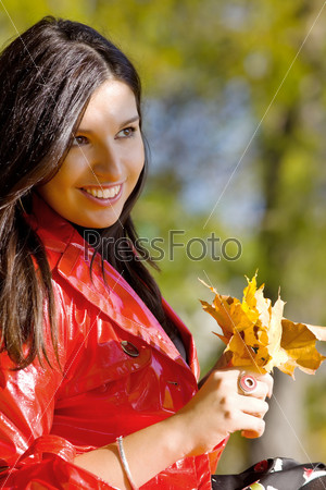 Молодая женщина в осеннем парке с желтыми листьями в руке