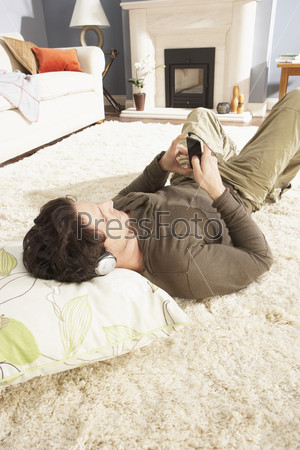 Man Listening To MP3 Player On Headphones Relaxing Laying On Rug At Home