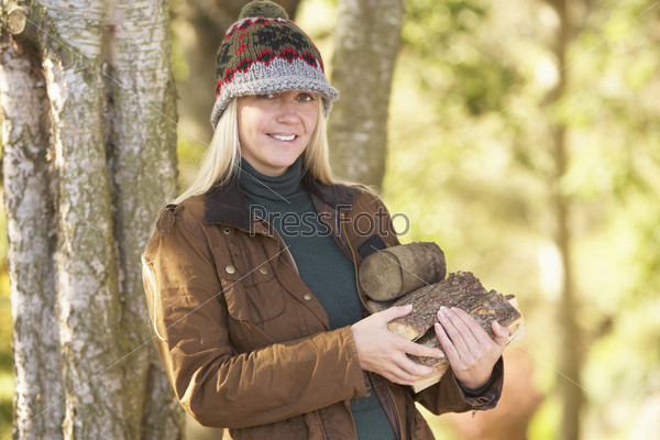 Woman Outdoors In Autumn Woodland Gathering Logs, stock photo