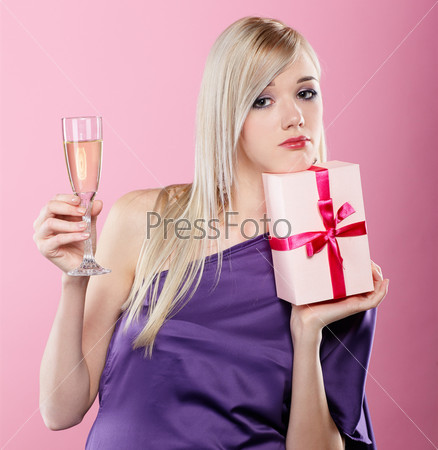 portrait of beautiful blonde party girl looking upset with birthday gift box and glass of champagne on pink