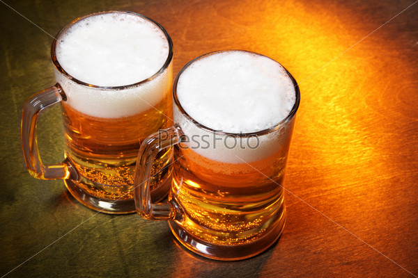 Кружки пива с пеной на деревянном столе