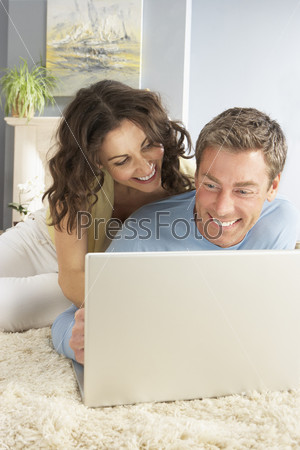 Couple Using Laptop Relaxing Laying On Rug At Home