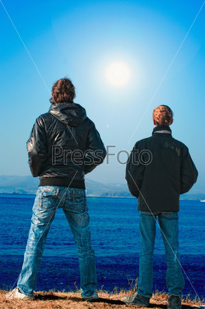 Two teenagers on an ocean coast looking afar