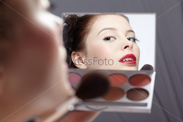 rear portrait of beautiful slavonic brunette girl making up. Face with brush reflects in toner box\'s mirror.