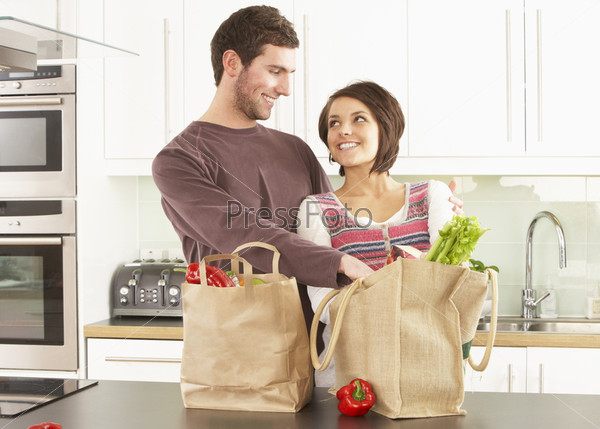 Young Couple Unpacking Shopping In Modern Kitchen