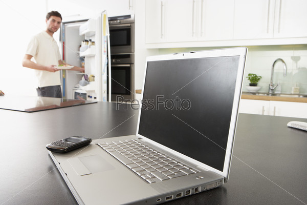 Young Man Fixing Snack In Kitchen With Laptop In Modern Kitchen