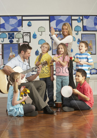Teachers Playing Guitar With Pupils Having Music Lesson In Classroom