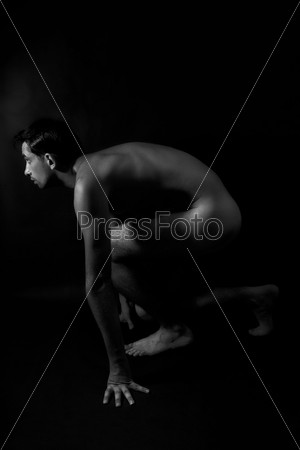 Nude male athlete preparing for the start on black background