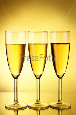 Three glasses of champagne over yellow background, stock photo