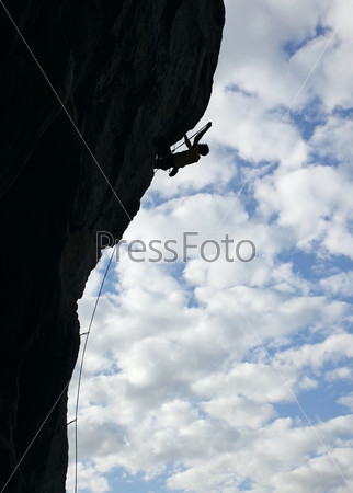 Silhouette of rock climber climbing an overhanging cliff with cloudy sky background