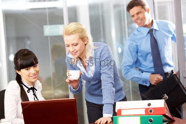 Two businesswomen looking at a laptop and a businessman entering
