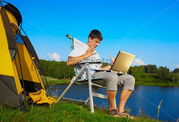 expression portrait of angry man with laptop sitting in folding chair near camp tent outdoors