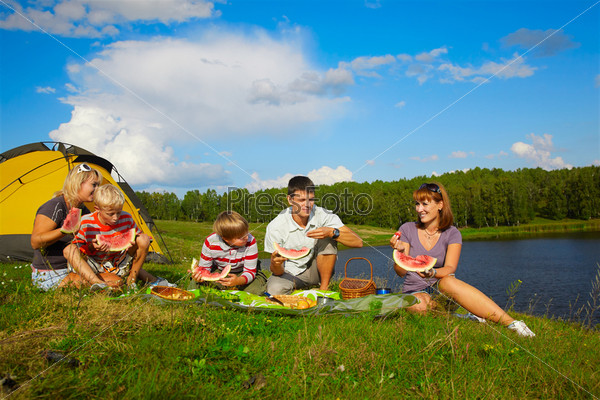 outdoor portrait of happy families enjoying watermelon at the picnic near camp tent